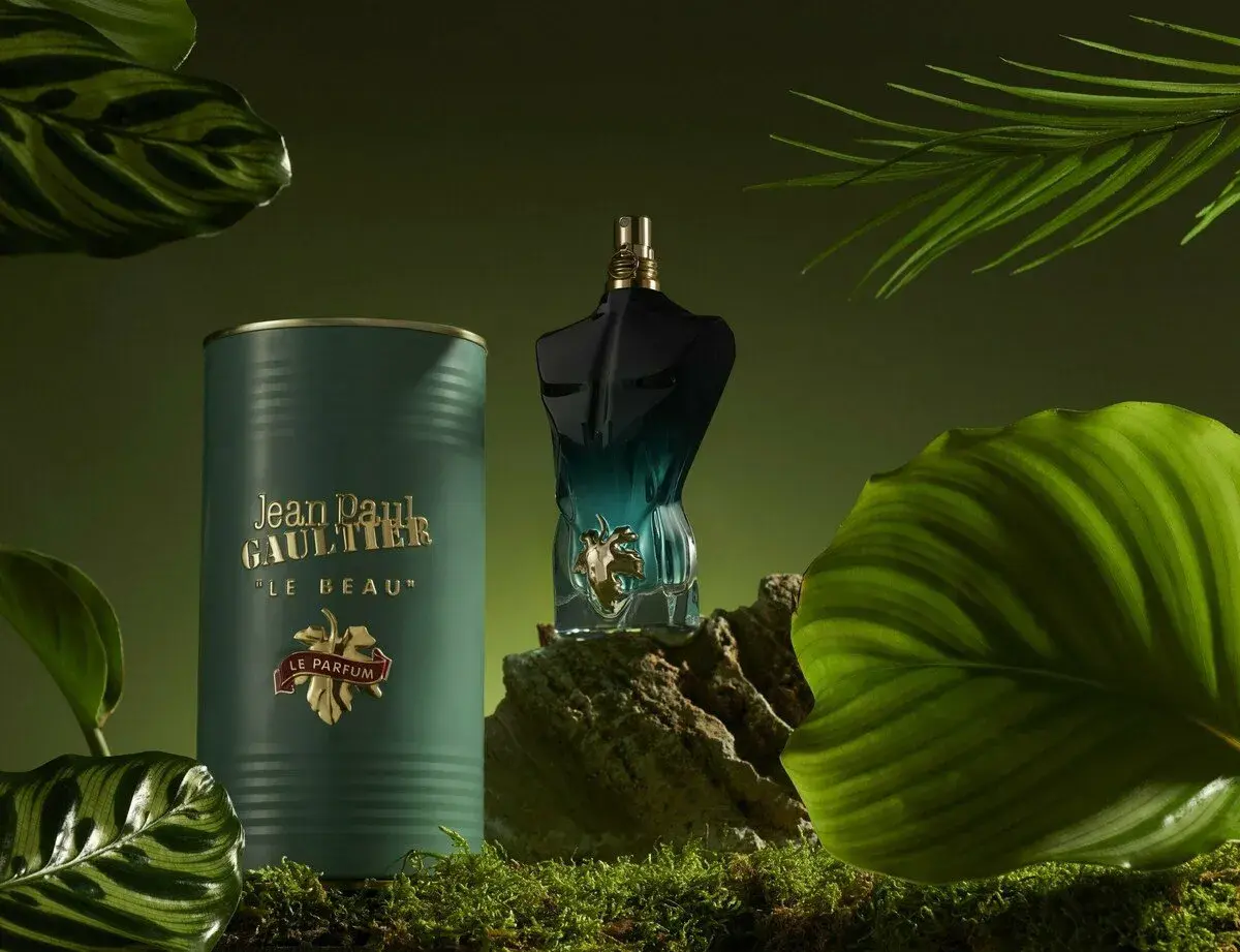 Flakon perfum Jean Paul Gaultier Le Beau Le Parfum w otoczeniu zielonych liści i mchu.