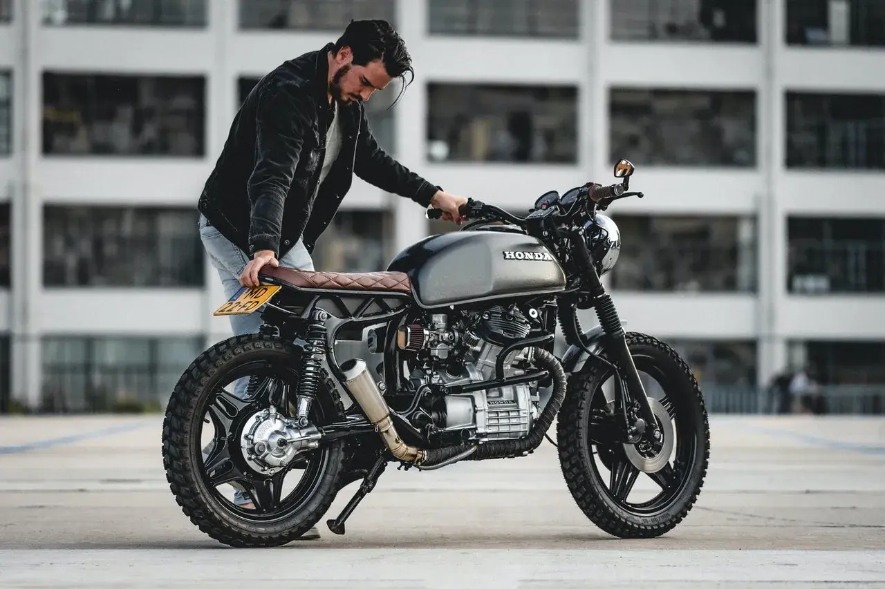 Uomo con moto custom grigia. La sella in pelle marrone ha una **godronatura** a rombi.