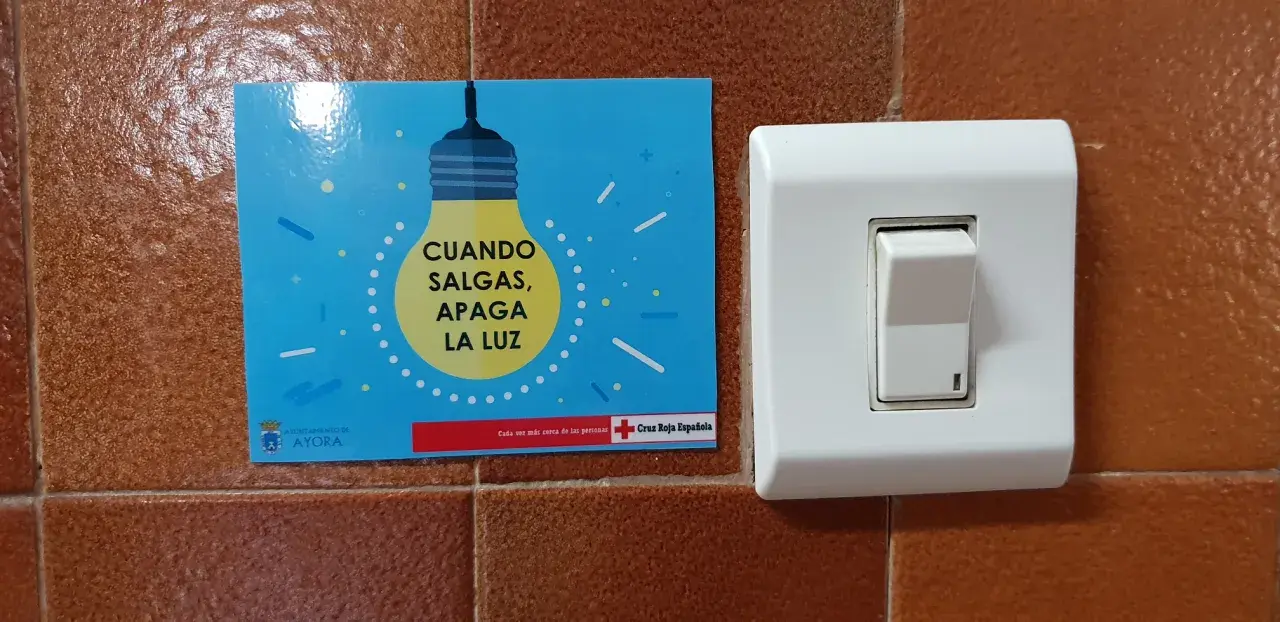 Un cartel azul con una bombilla amarilla y el texto "CUANDO SALGAS, APAGA LA LUZ" junto a un interruptor blanco.