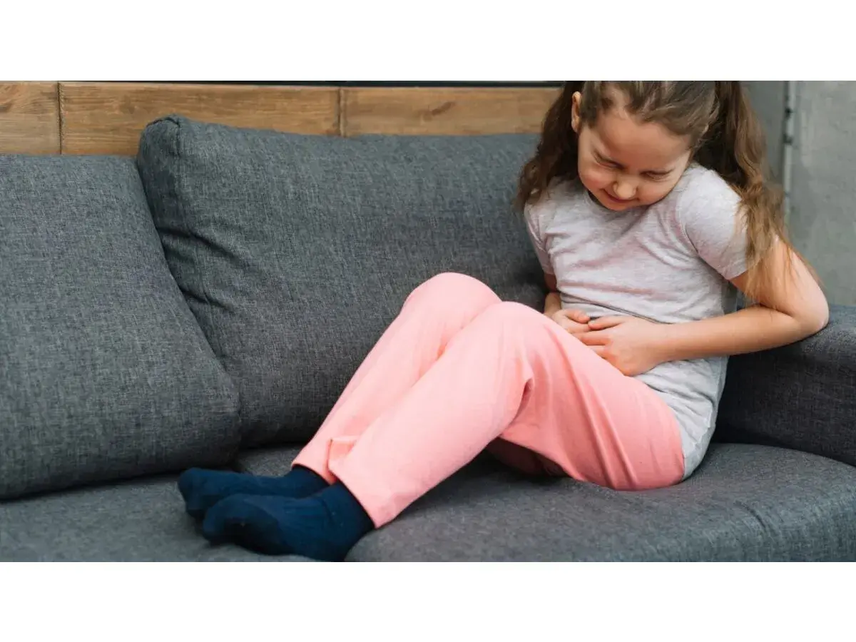 Bambina sul divano con le mani sulla pancia, che mostra i sintomi di appendicite.