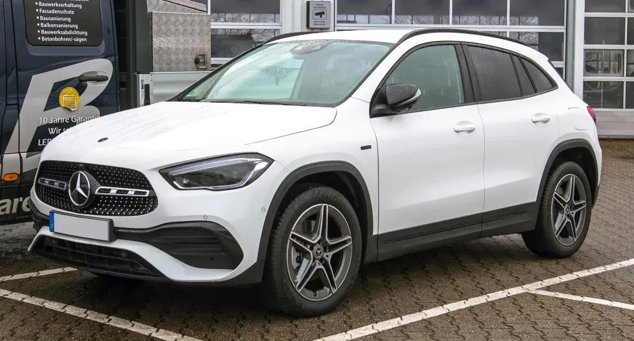 Biały Mercedes GLA, kompaktowy SUV, zaparkowany na mokrym parkingu. Jego wymiary idealnie pasują do miejskiej dżungli.