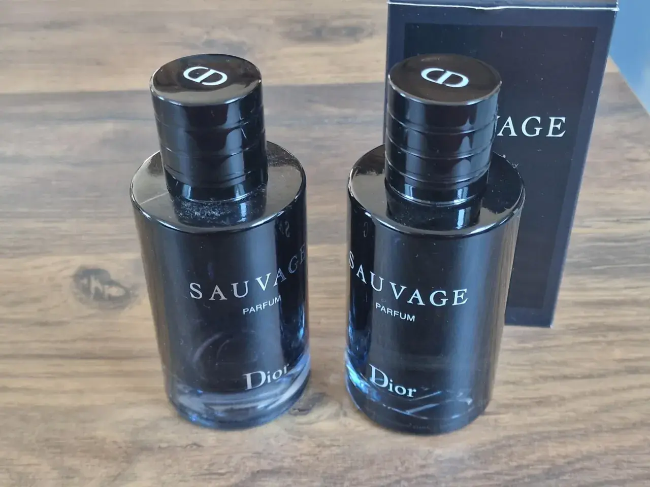 Dwa flakony Dior Sauvage Parfum 100ml, każdy z czarną zakrętką z logo CD.