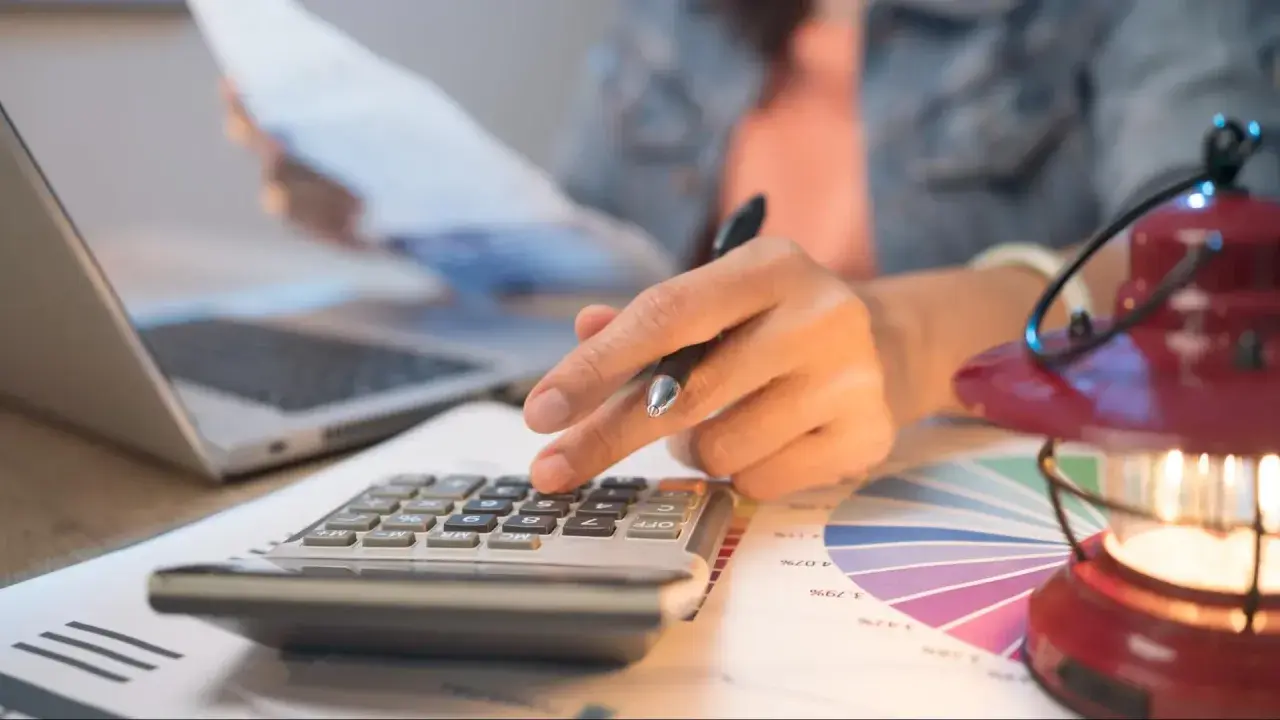Persona calcula con calculadora y portátil, revisando gráficos. Quizás planeando una hipoteca puente Santander.