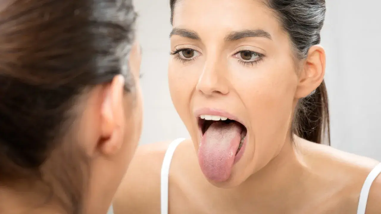 Mujer revisa su lengua en el espejo, buscando una lengua sana.
