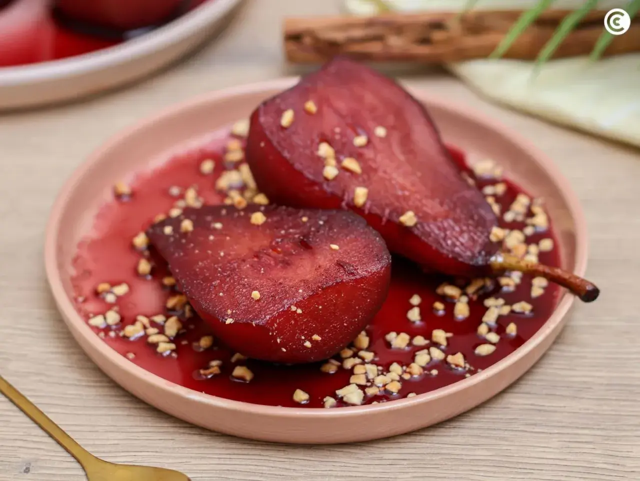 Peras al vino, tiernas y brillantes, servidas en un plato rosa con trocitos de nuez y un sirope rojo intenso.
