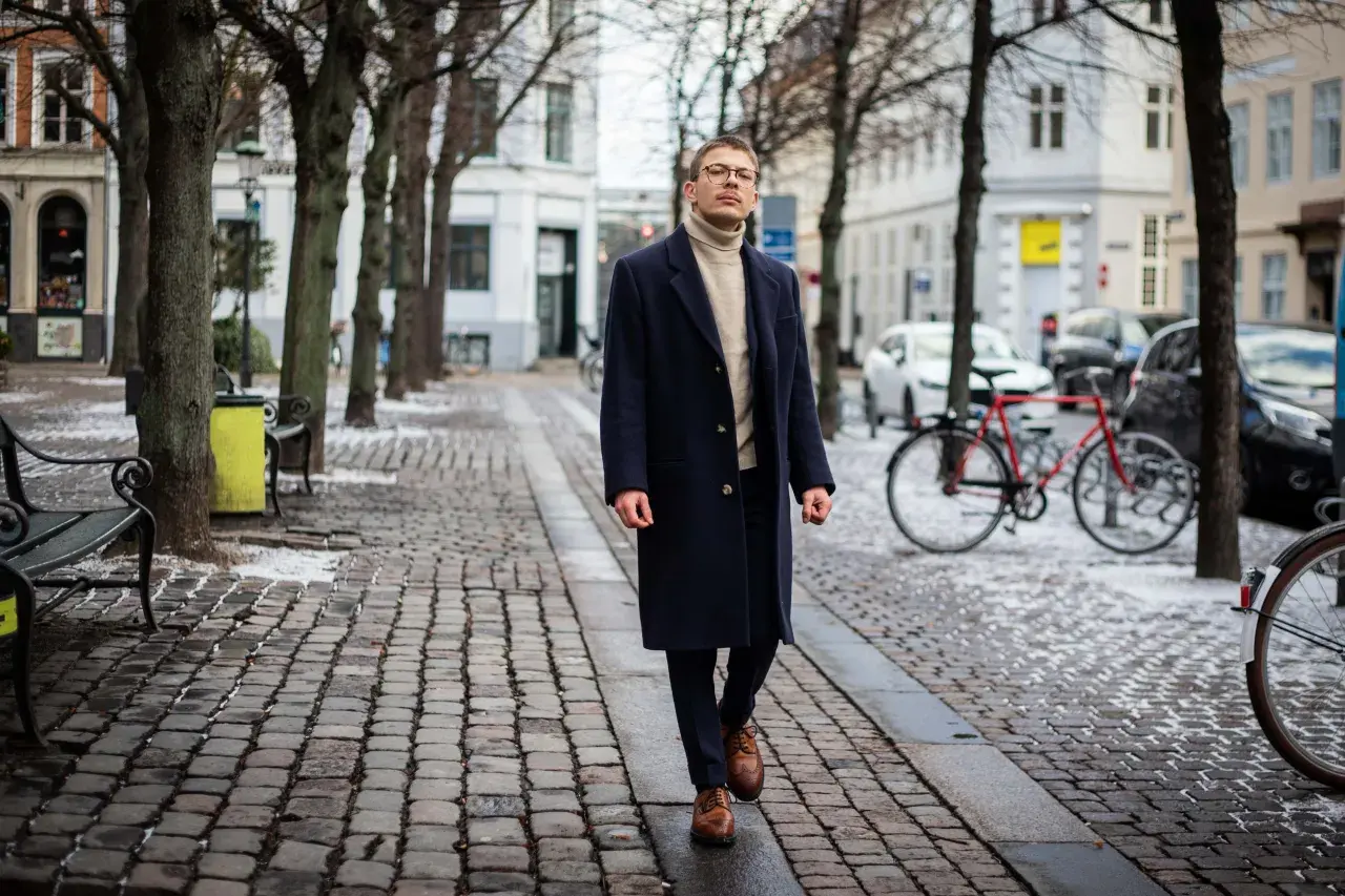 Elegancki mężczyzna w granatowym płaszczu i golfie spaceruje po zimowej ulicy. Stylowe granatowy płaszcz stylizacje na chłodne dni.