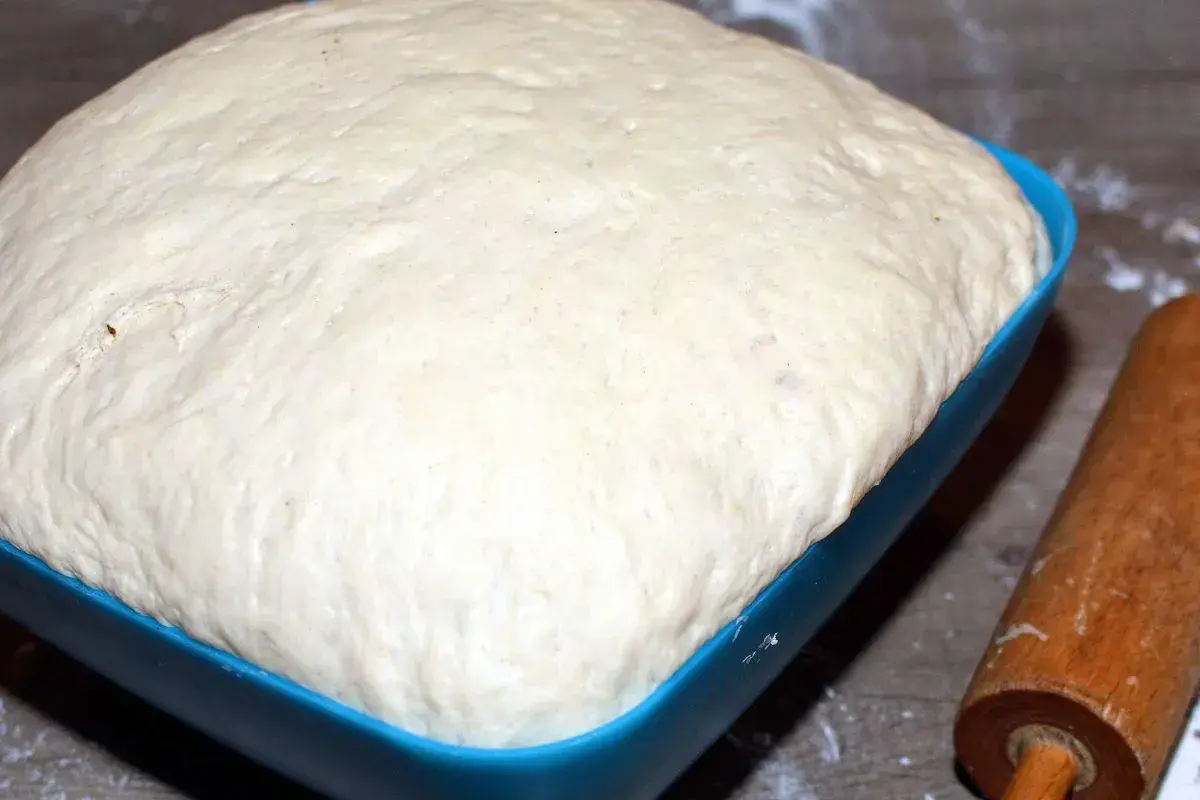 Puszyste ciasto na pizzę w niebieskiej misce, gotowe do pieczenia. Dowiedz się, jak rozmrozić ciasto na pizzę, by było idealne.