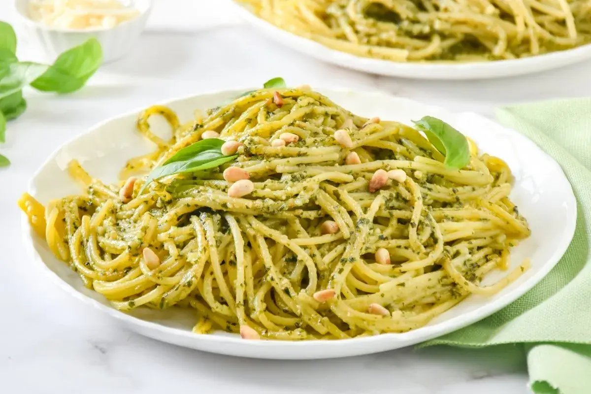 Un plato de espaguetis al pesto, cubierto con piñones y hojas de albahaca fresca.