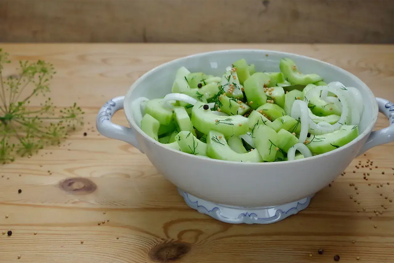 Schneide Gurken für ein schnelles Rezept: Gurkensalat mit Zwiebeln, Dill und Senfkörnern in einer Schüssel.