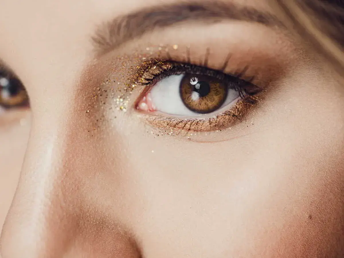 Un œil marron orné d'un maquillage soirée doré scintillant, parfait pour briller toute la nuit.