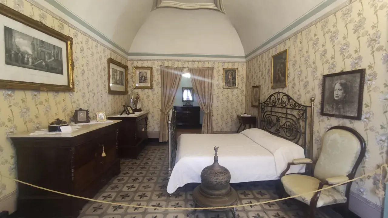 Camera da letto nella casa di d'Annunzio, con carta da parati floreale, letto in ferro battuto e mobili d'epoca.