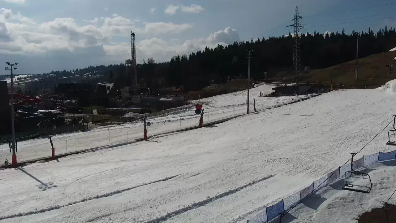 Widok z białka tatrzańska webcam na ośnieżony stok narciarski z wyciągiem krzesełkowym i wieżą w tle.