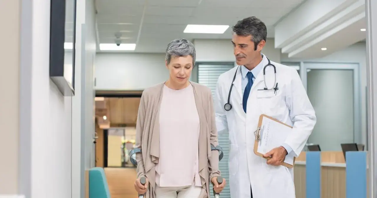 Lekarz wspiera pacjentkę po urazie, która porusza się o kulach. Postęp w leczeniu traumatologii jest widoczny.