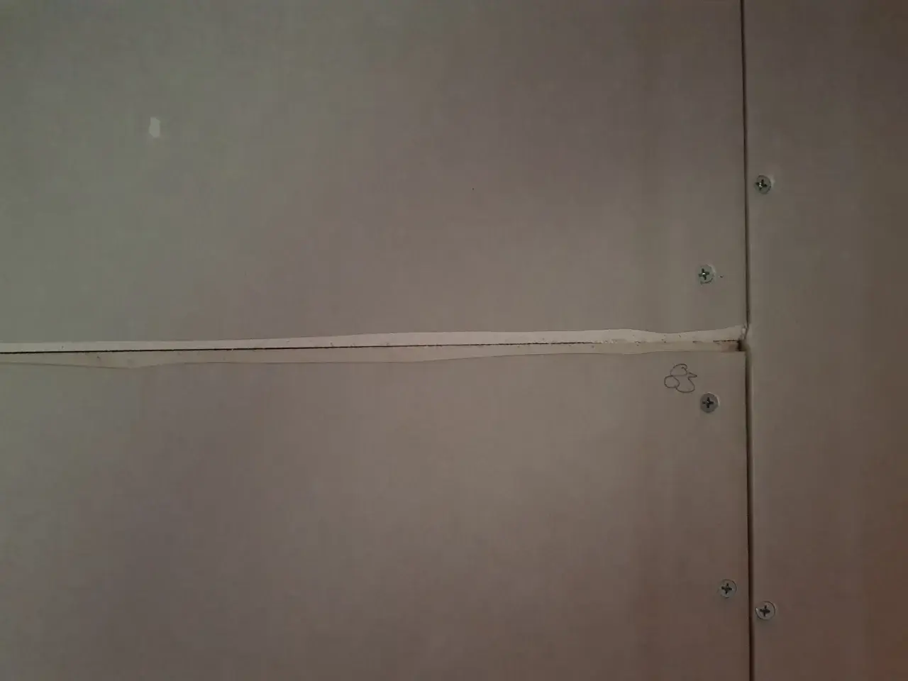 Närbild på gipsskivor där skarvarna spacklas för att skapa en jämn yta. Skruvarna syns tydligt.