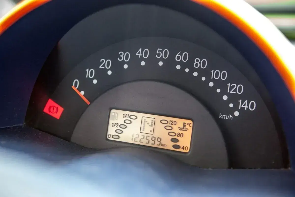 Cruscotto auto con tachimetro, indicatore carburante e spia freno a mano accesa. Chilometraggio 122599 km.