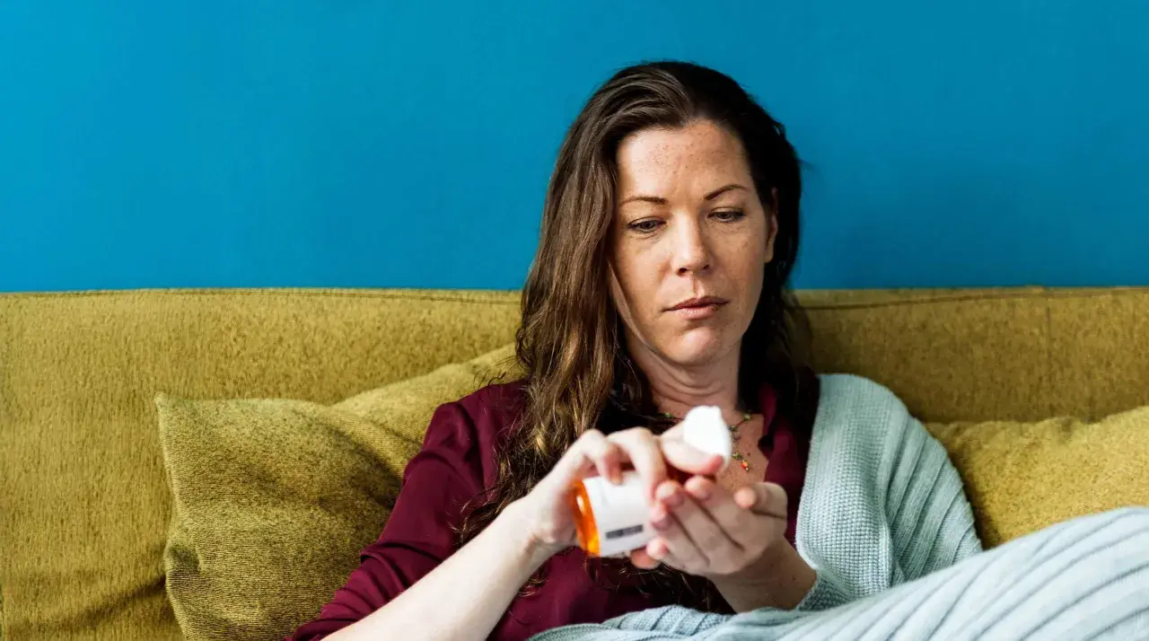 Vrouw neemt medicatie, hopend dat werkt bachbloesem echt. Ze zit op een bank met een deken.