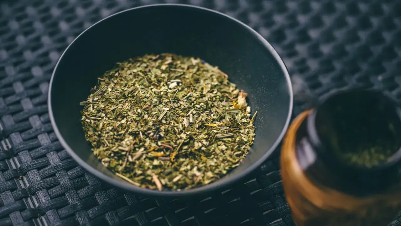 Suszone liście i gałązki, z których jest yerba mate, w czarnej miseczce obok tykwy.