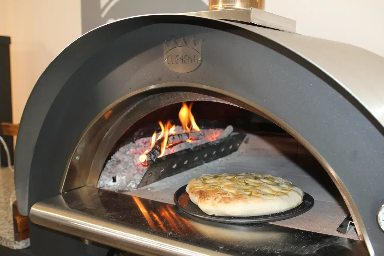 Una crescia dorata pronta per essere infornata in un forno a legna Clementi, con fiamme vive che creano l'atmosfera perfetta per la ricetta.
