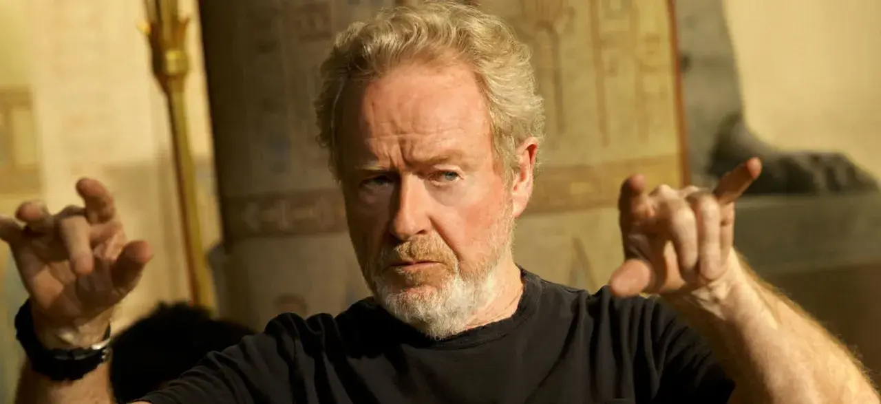 Reżyser Ridley Scott, znany z kultowych filmów, gestykuluje na tle starożytnych dekoracji.
