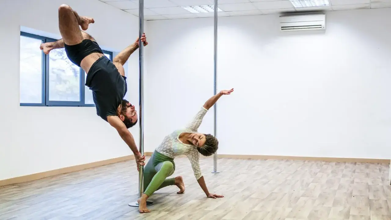 Mężczyzna w powietrzu, kobieta na podłodze. Ich taniec na słupie, niczym kołyska pole dance, tworzy hipnotyzującą choreografię.