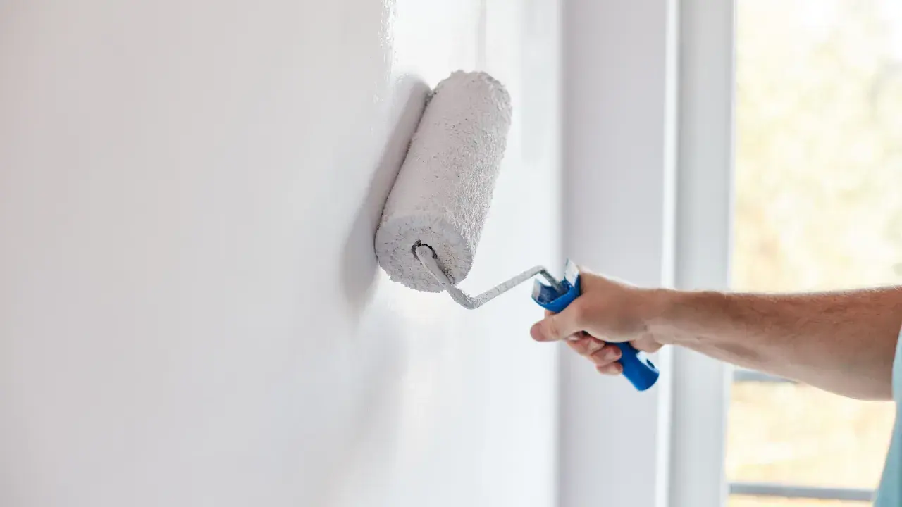 Mano aplica pintura aterciopelada blanca a una pared con un rodillo.