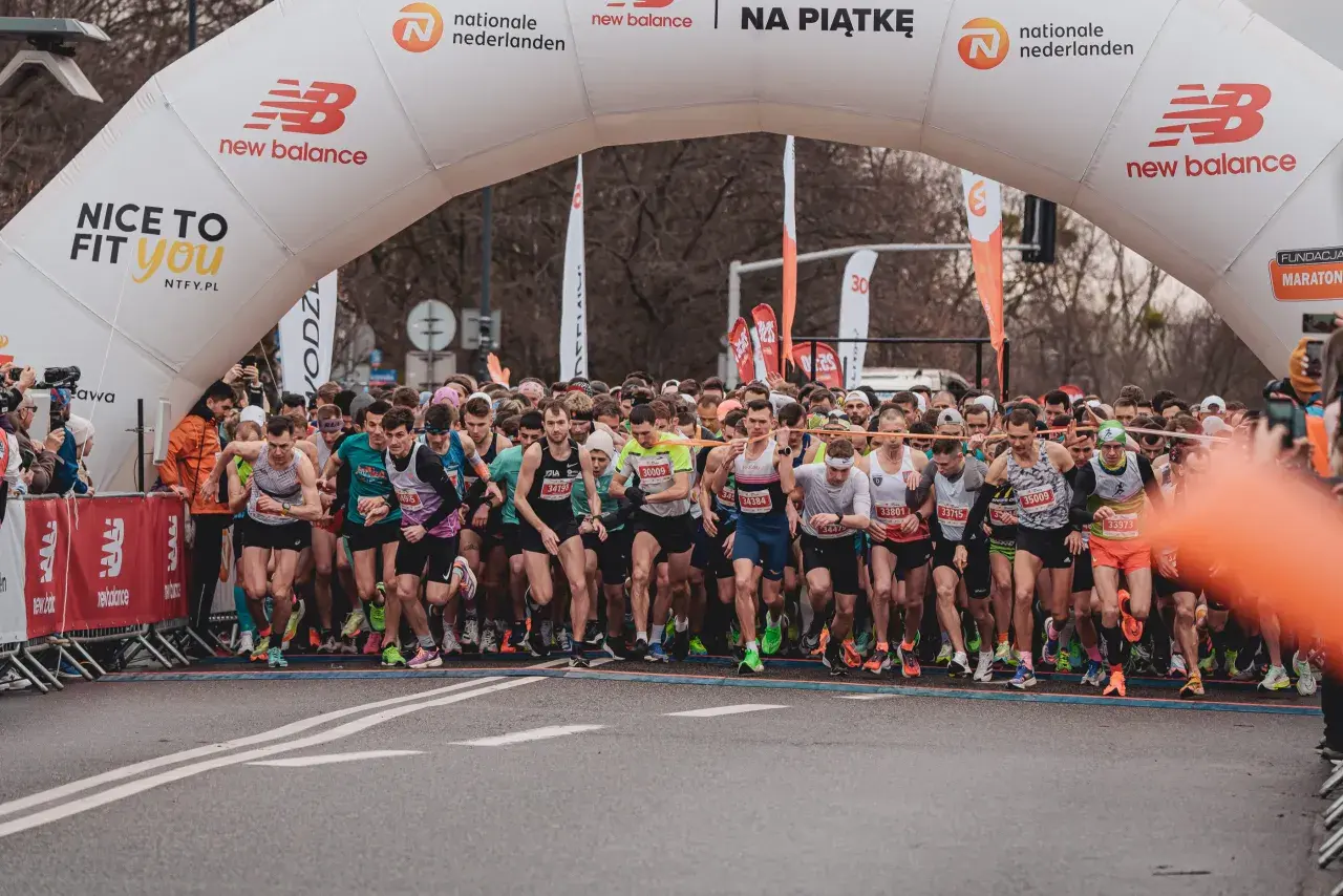 Start biegu na 10 km. Tłum biegaczy pod łukiem startowym New Balance, gotowi do rywalizacji.