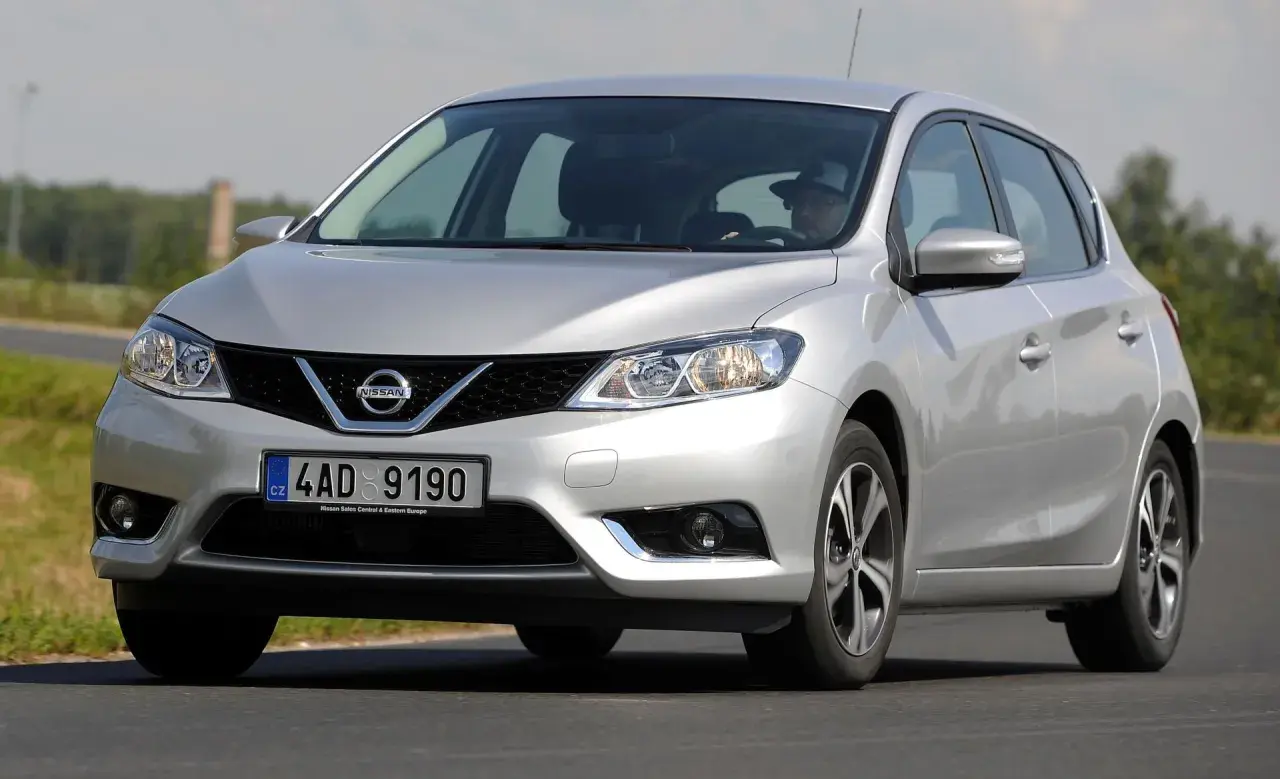 Srebrny Nissan Pulsar w ruchu drogowym. Kierowca w kapeluszu za kierownicą. Wiele pozytywnych nissan pulsar opinie.