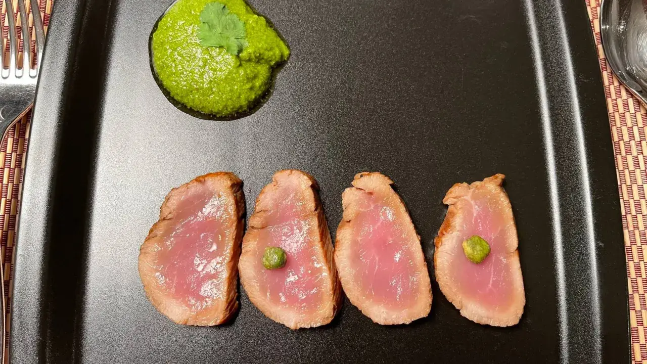 Cuatro lonchas de tataki de salmón con un toque de salsa verde y alcaparras, servidas en plato negro.