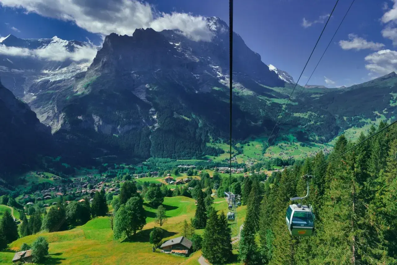 Widok z kolejki linowej na dolinę Grindelwald, z górami w tle i zielonymi łąkami.
