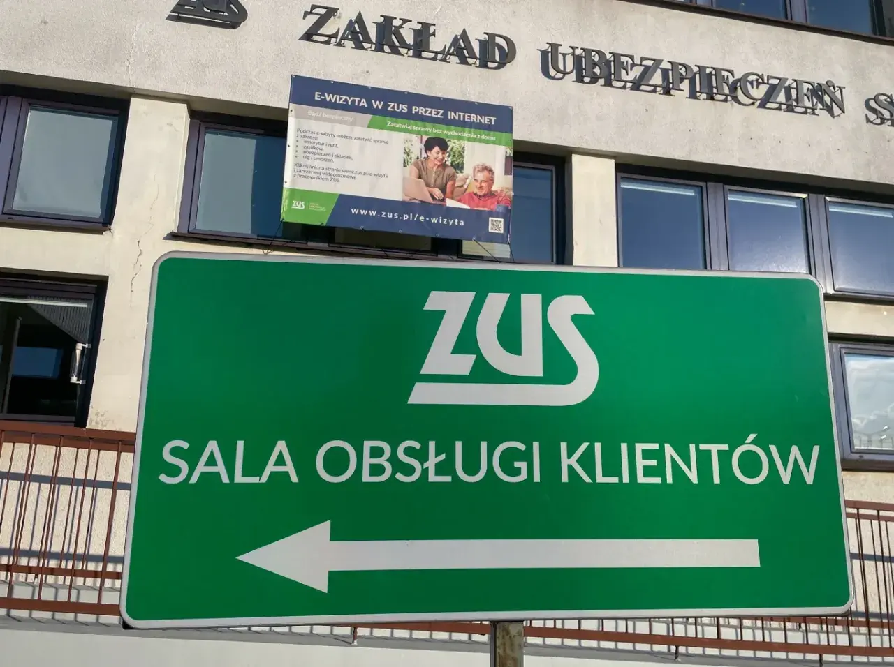 Zielony znak z logo ZUS i napisem "SALA OBSŁUGI KLIENTÓW" wskazuje drogę do placówki zarządzania socjalnego ubezpieczenia.