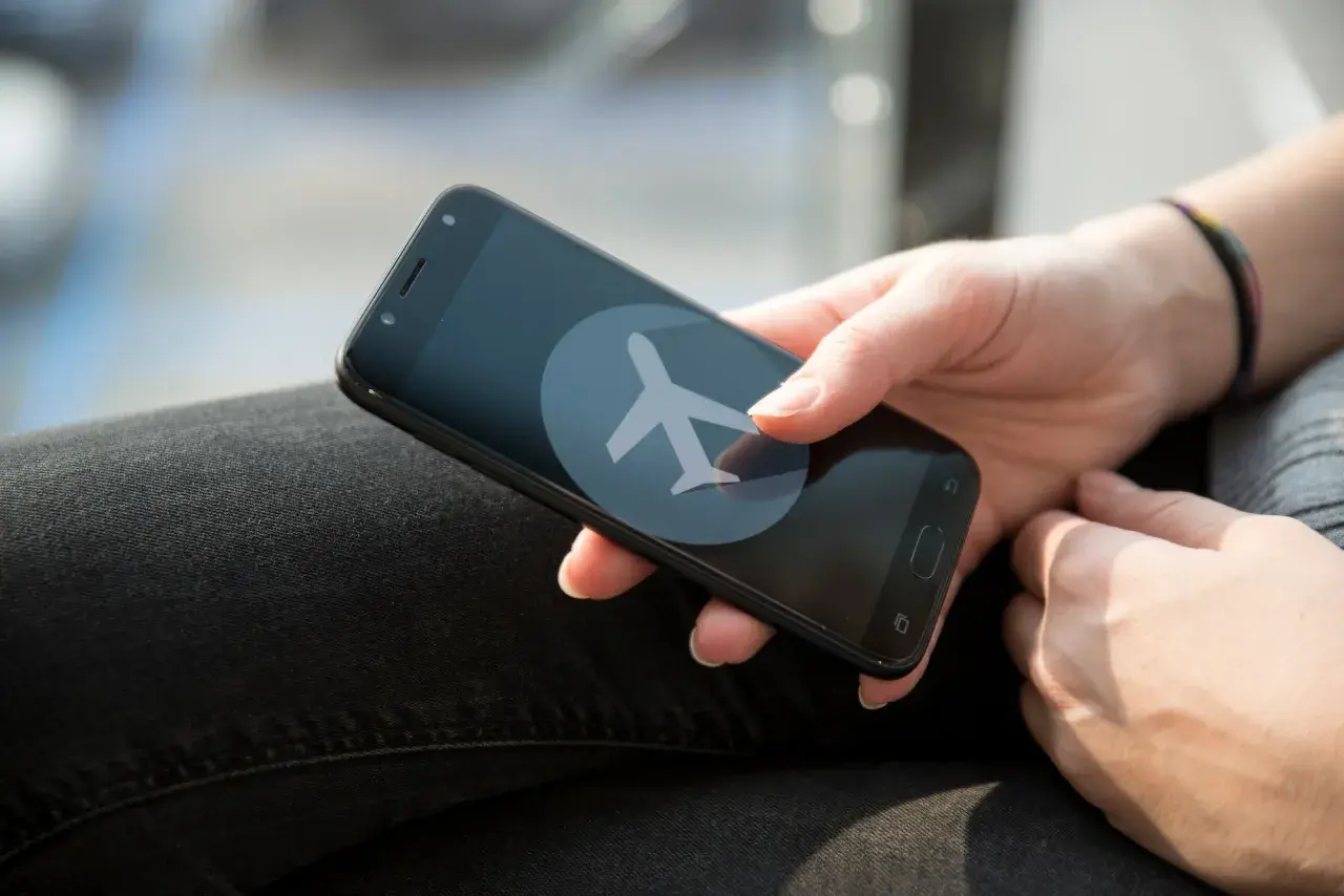 Dłoń trzyma smartfon z ikoną samolotu. Zastanawiasz się, czy w trybie samolotowym działa budzik?