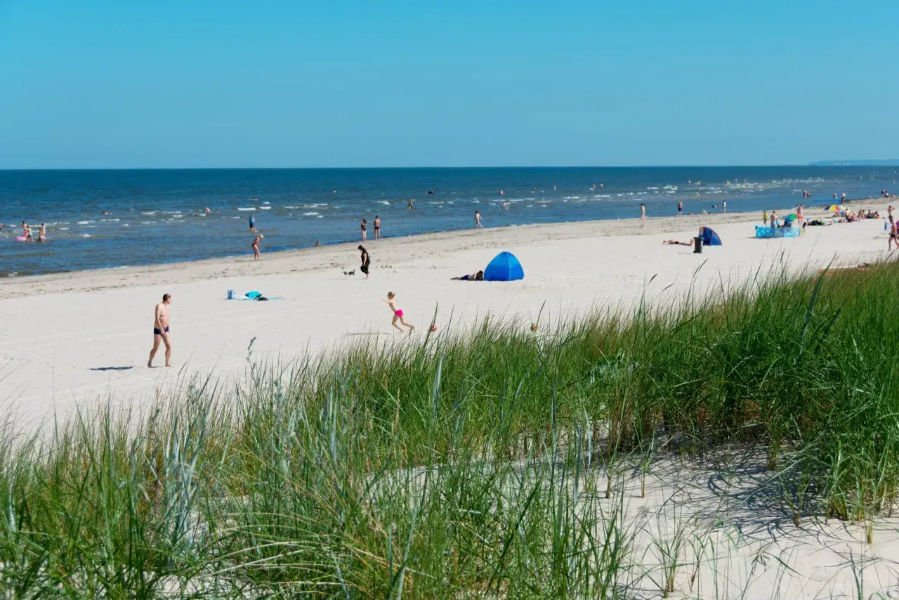 Menschen genießen einen sonnigen Tag am Strand der Ostsee. Nach der Fahrt mit dem Zug von Berlin ist dies eine willkommene Erfrischung.
