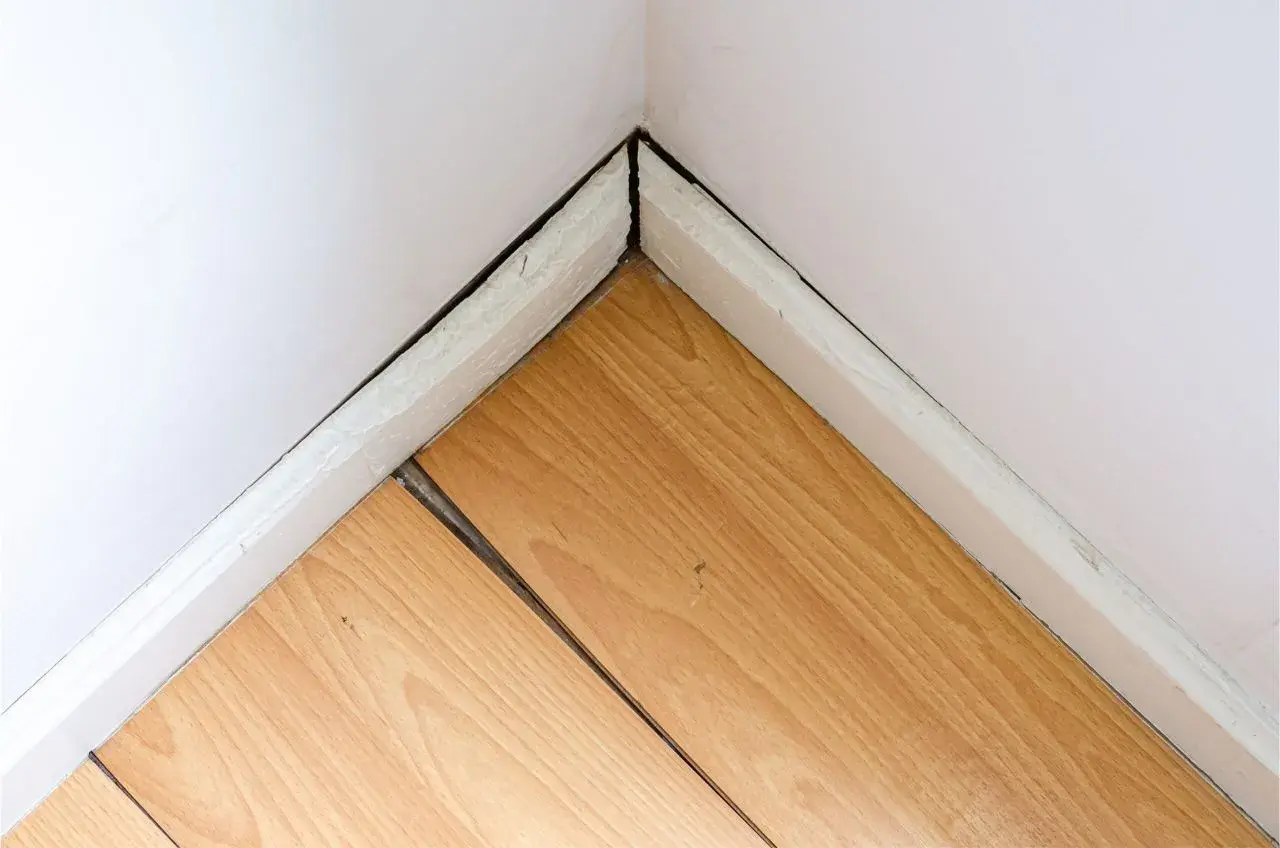 Esquina de habitación con suelo laminado hinchado por agua, mostrando las tablas separadas y levantadas.
