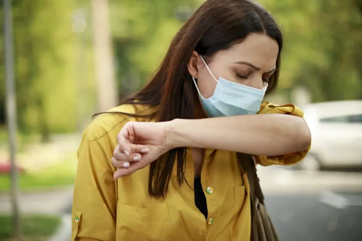 Mujer con mascarilla quirúrgica para que sirve, tose en el codo para evitar contagios.