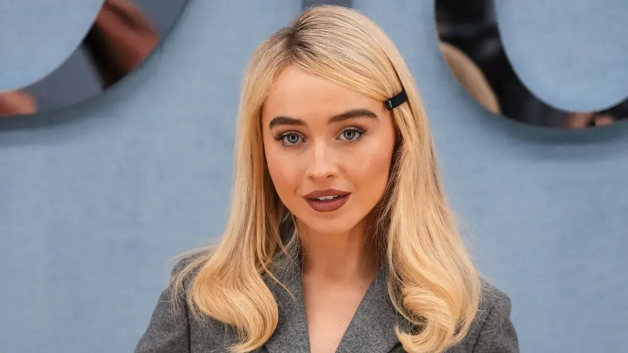 Mujer rubia con raya del pelo lateral, ojos azules y un clip negro en el cabello.