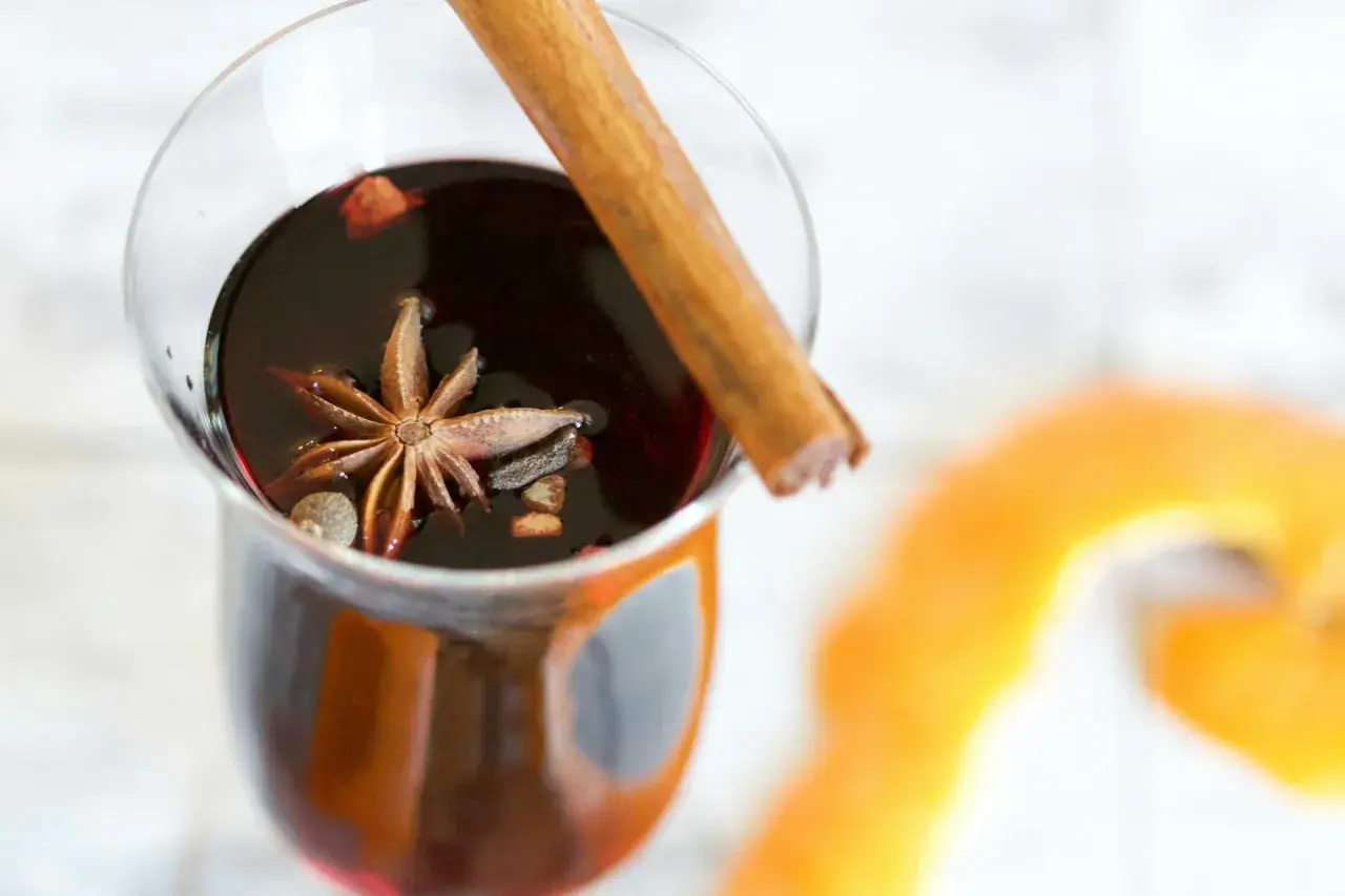 Un verre de vin chaud aux épices, parfait pour un marché de Noël. Une étoile de badiane et un bâton de cannelle flottent dans le liquide sombre.