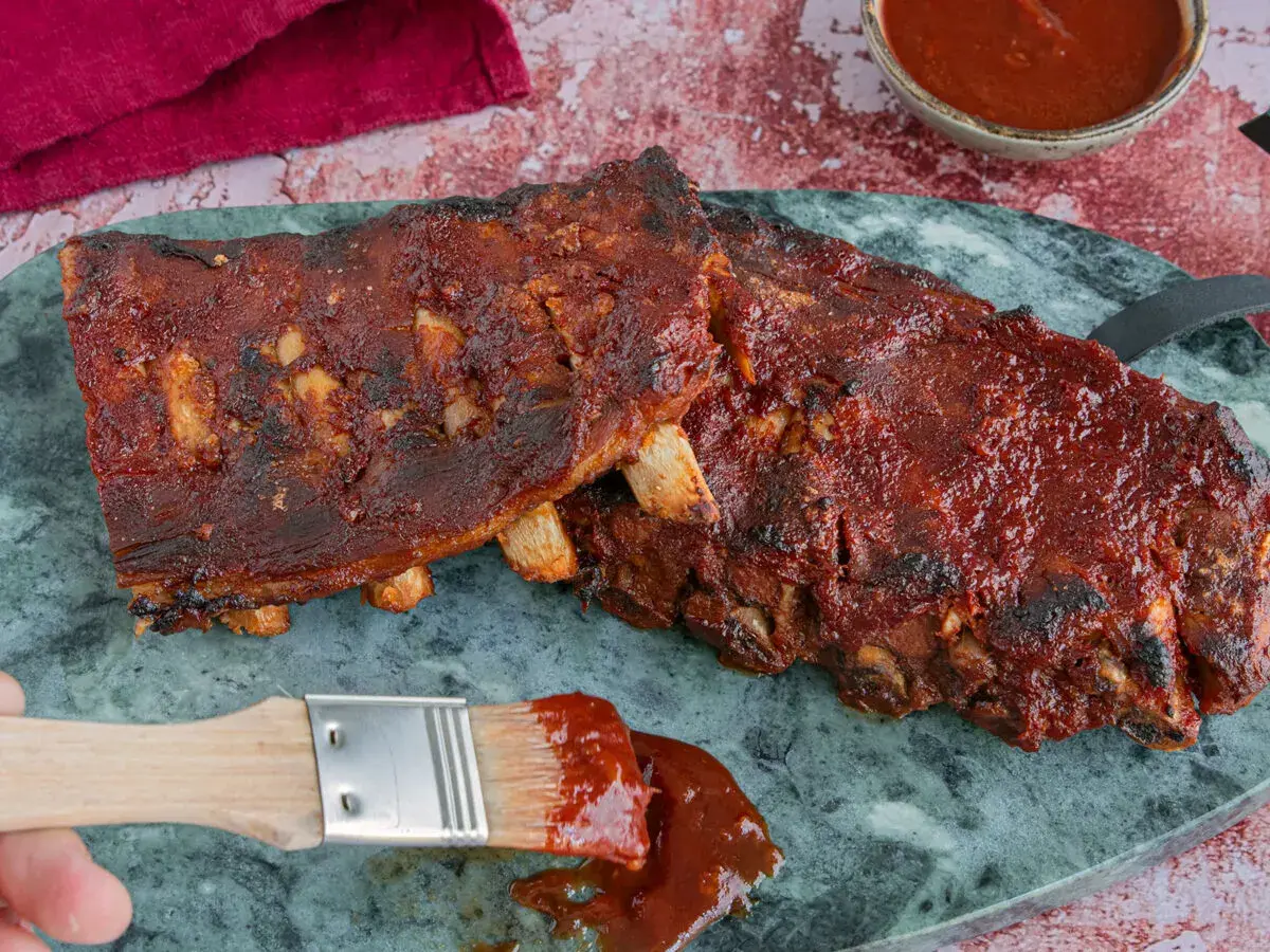 Saftige Spareribs sous vide, glasiert mit BBQ-Sauce. Ein Pinsel mit Sauce liegt daneben.