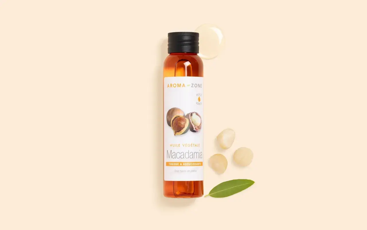 Flacon d'huile de macadamia, ses bienfaits pour la peau sont nombreux. Noix et feuille à proximité.