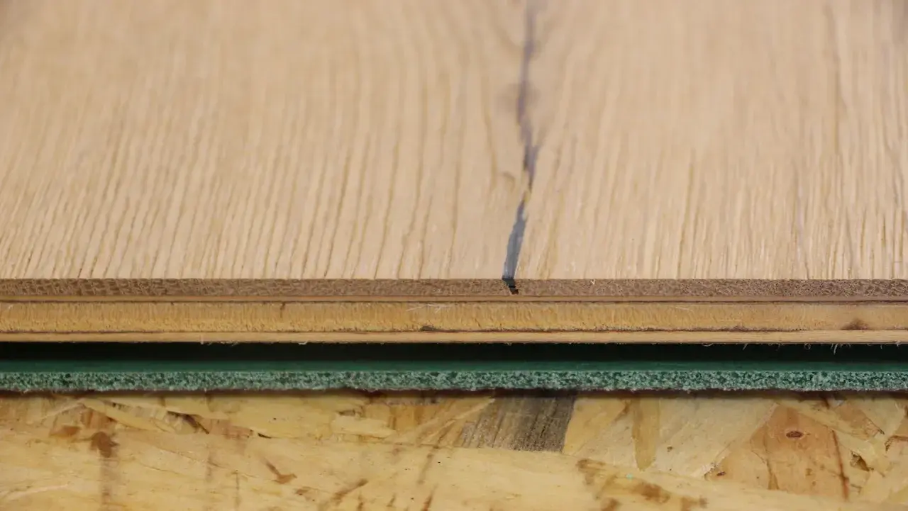 Detailaufnahme von Holzschichten und grüner Trittschalldämmung, bereit für das Parkett verlegen.