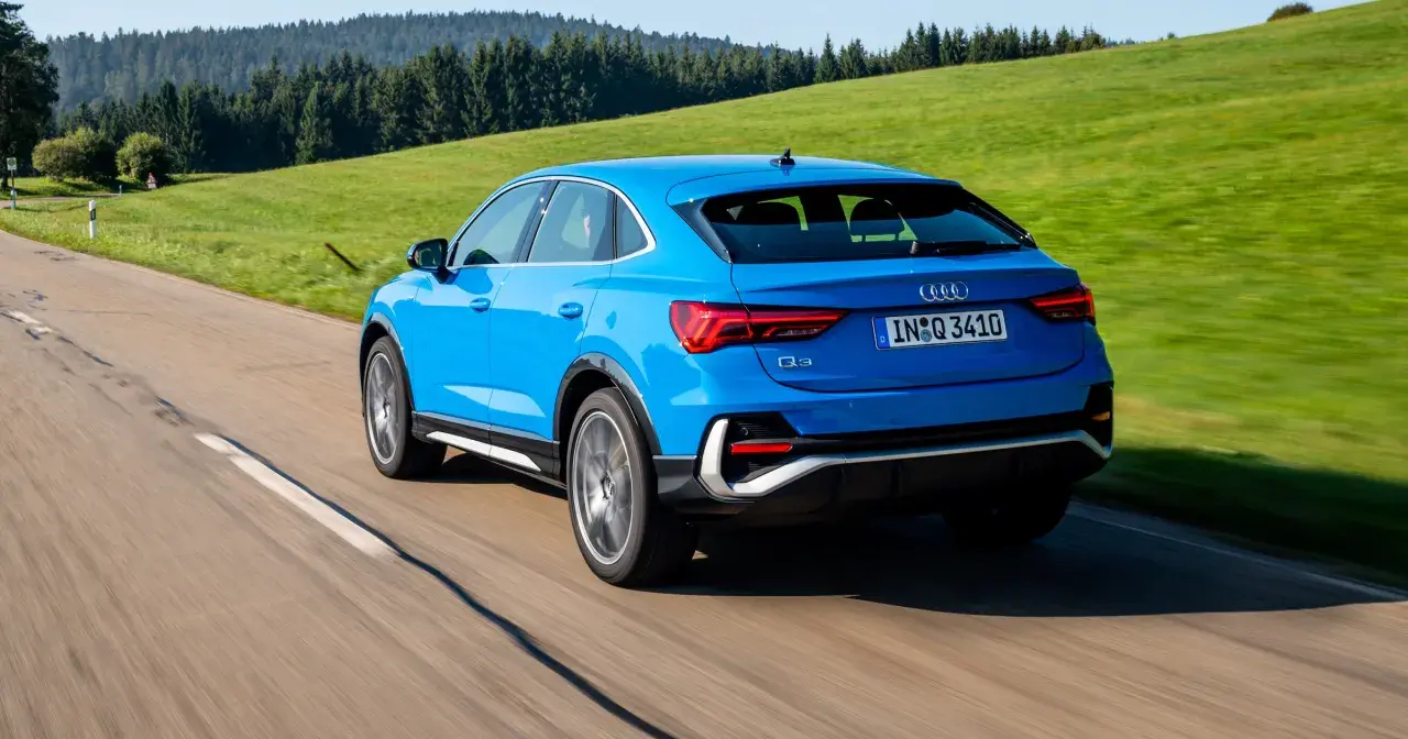 Niebieskie Audi Q3 Sportback jedzie po krętej drodze wśród zielonych wzgórz. Poznaj jego wymiary.