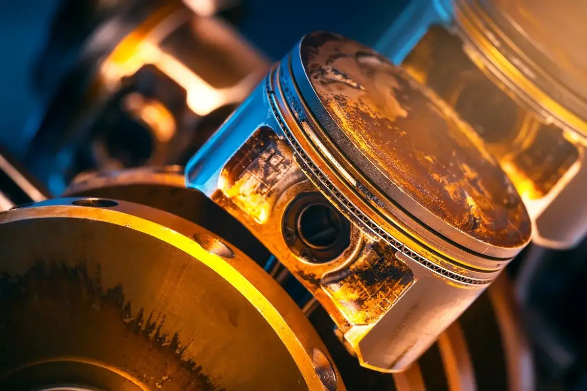 Zbliżenie na tłok silnika z widocznym luzem pierścieni tłokowych. Metaliczne elementy silnika w ciepłym oświetleniu.