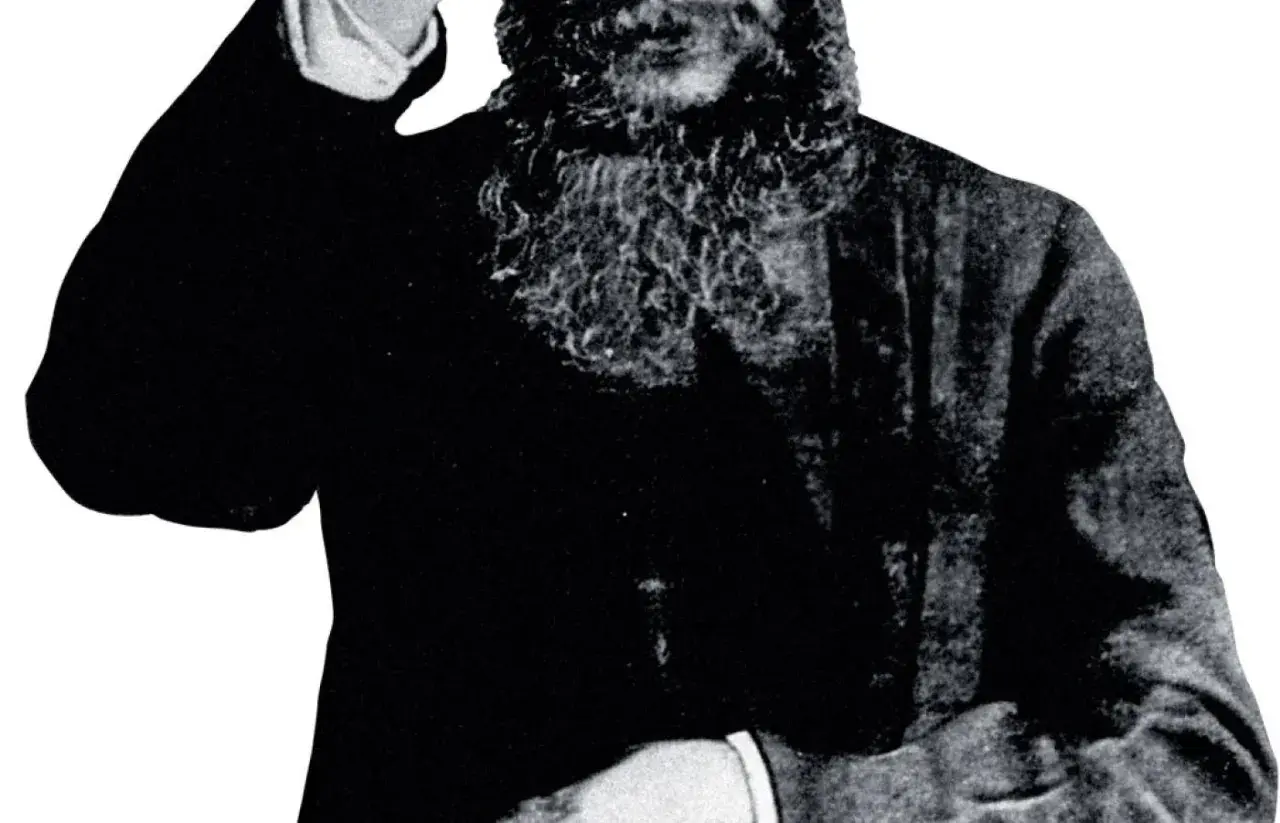 Grigorij Rasputin, z charakterystyczną brodą, wznosi rękę w geście błogosławieństwa lub pozdrowienia.