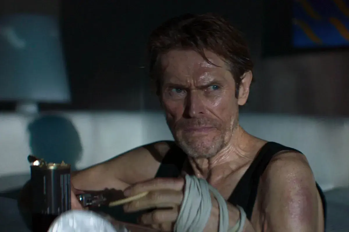 Willem Dafoe z papierosem w dłoni, z bandażami na ręce, w scenie sugerującej dobry thriller psychologiczny film.