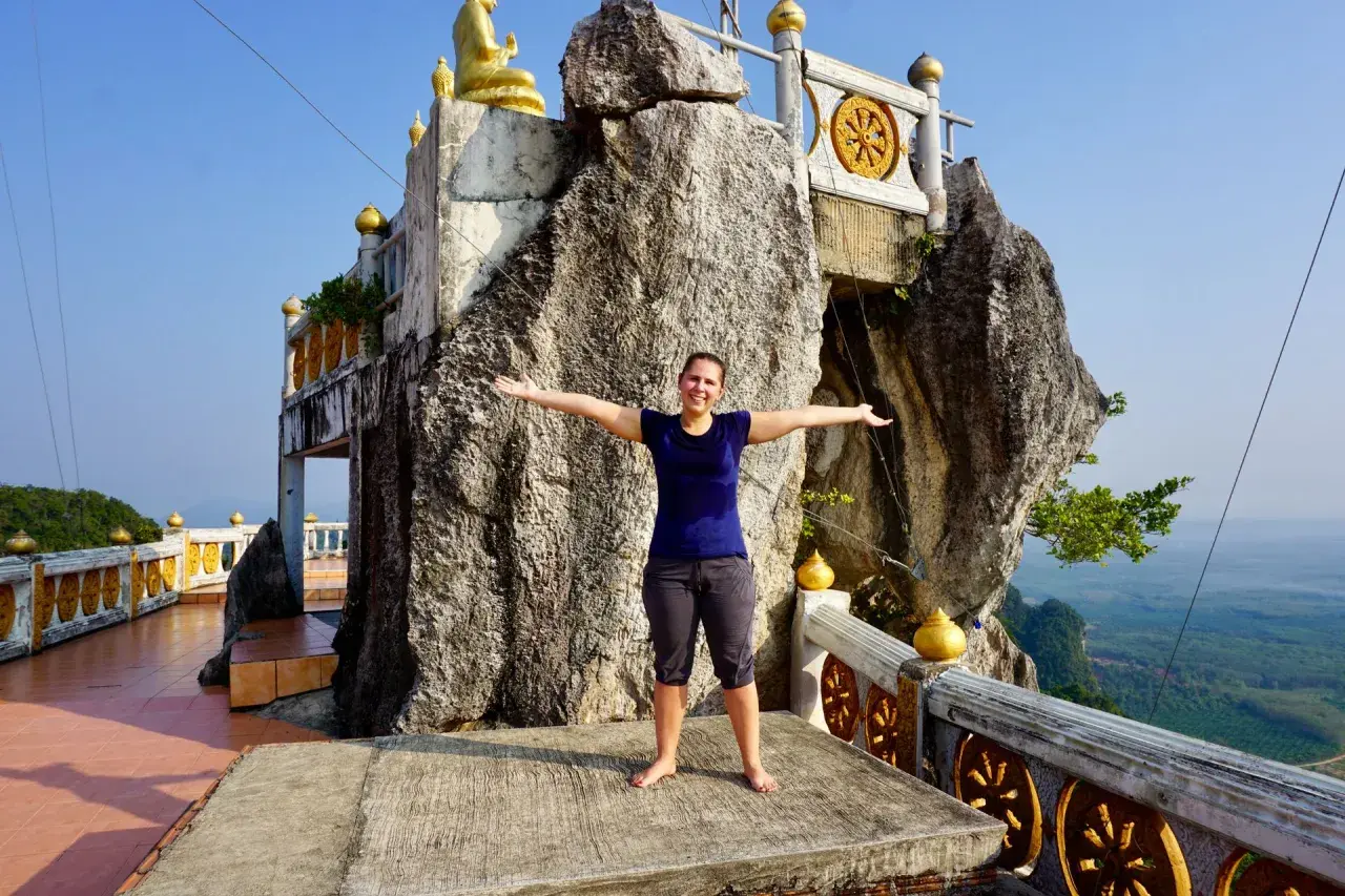 Frau steht vor einem Felsen, der wie ein Tigerhöhlentempel aussieht. Stufen führen zum Tempel.