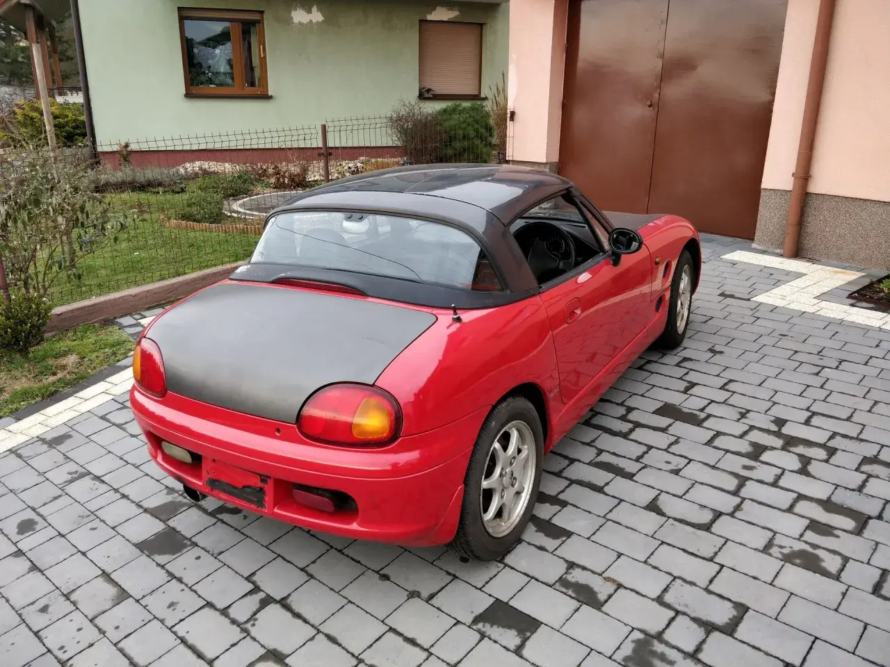 Czerwone Suzuki Cappuccino z czarnym dachem i maską stoi na podjeździe z kostki brukowej.