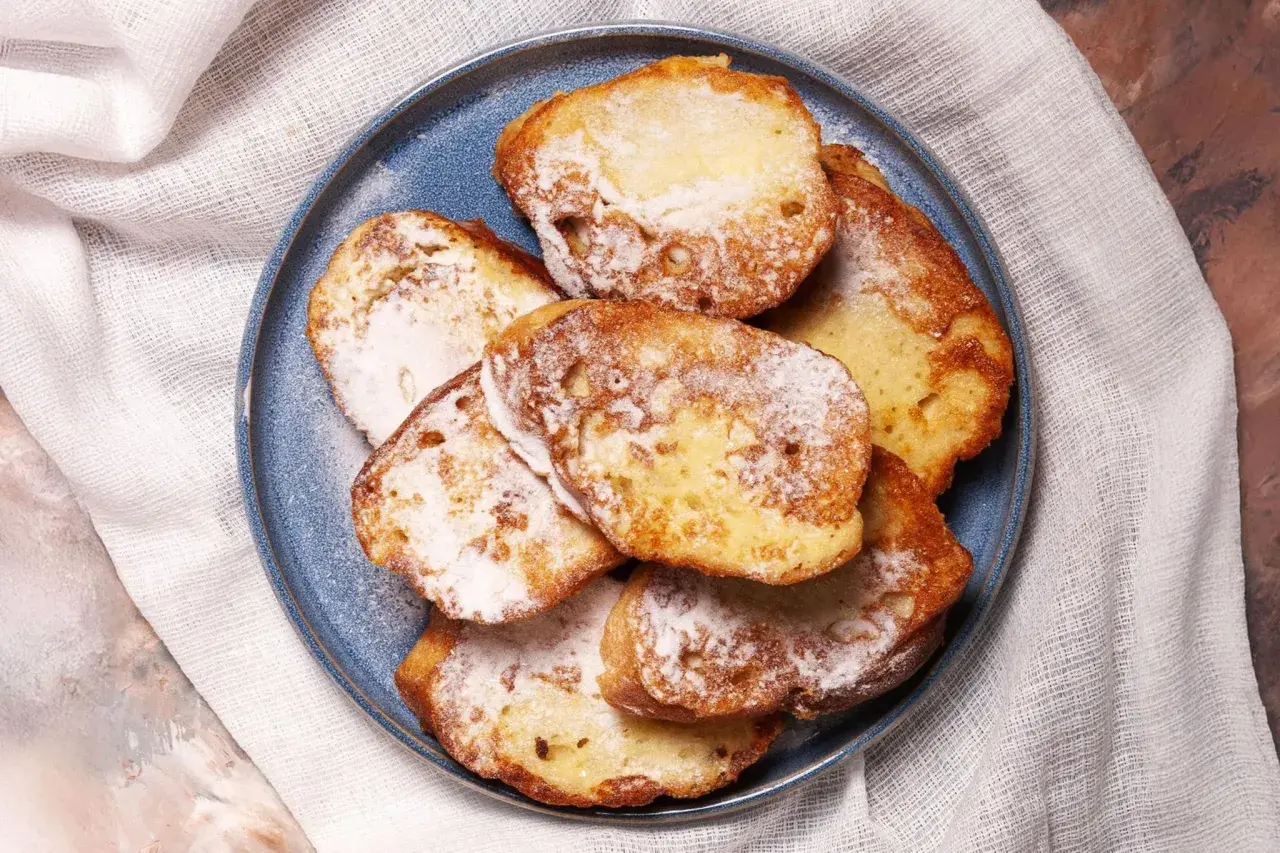 Armer Ritter, goldbraun gebacken und mit Puderzucker bestäubt, liegen auf einem blauen Teller.