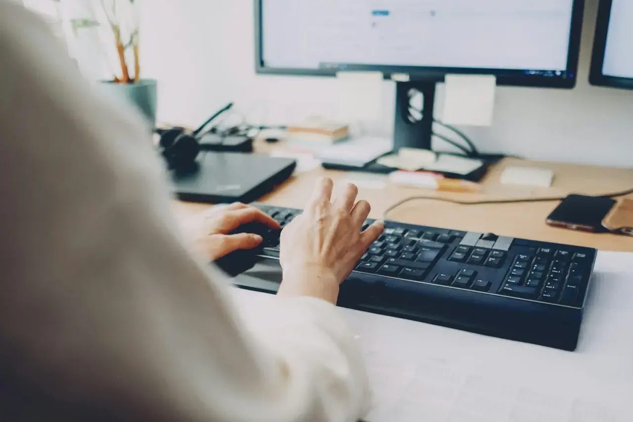 Dłonie piszą na klawiaturze, za nimi monitor. Szybkie załatwienie sprawy, może zwolnienie lekarskie online?