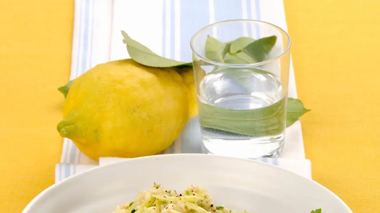 Un piatto di riso zucchine e limone, con un limone fresco e un bicchiere d'acqua.