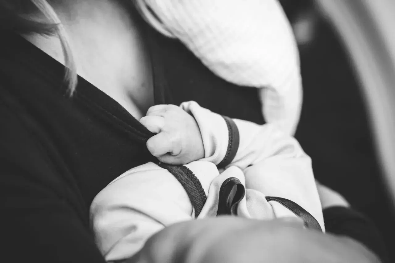 Dłoń noworodka czepia się ubrania mamy. Delikatne paluszki, mimo chwilowych baby blues, szukają bliskości.