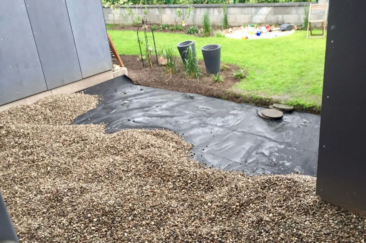 Baustelle für eine splitt terrasse mit Vlies und Kies. Im Hintergrund Rasen und Spielzeug.